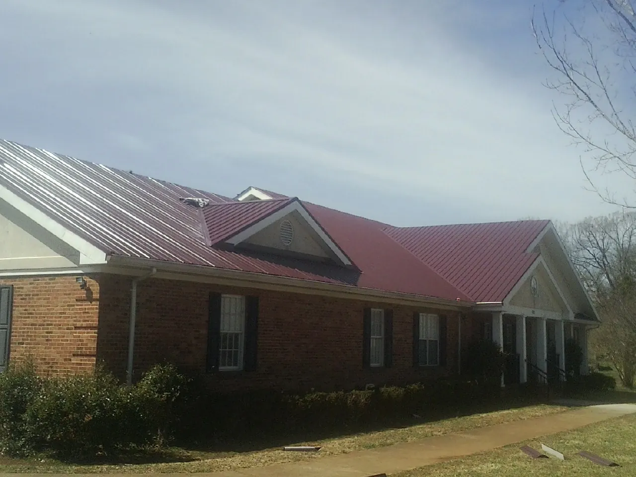 Red metal roof with gabled entries on a long brick building, from a Hail Damage Roof Repair job in Saltese