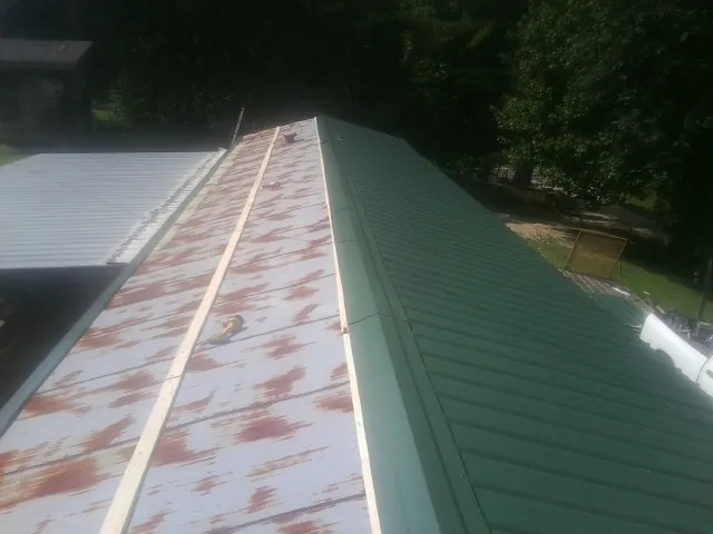 Old rusted panels beside newly installed green metal roofing — Wind Damage Roof Repair by Roofing Brothers in Saltese