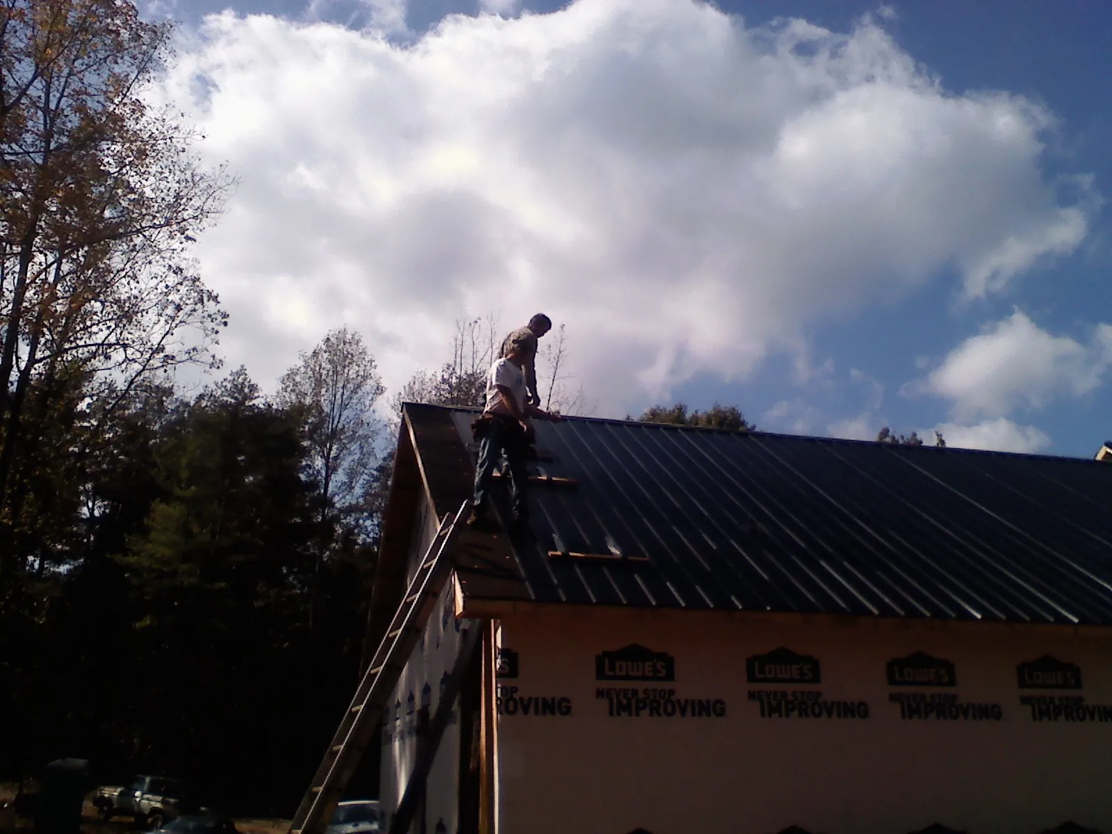 Roofer fastening dark metal panels high against a cloudy sky, from a Roof Inspection job in Saltese